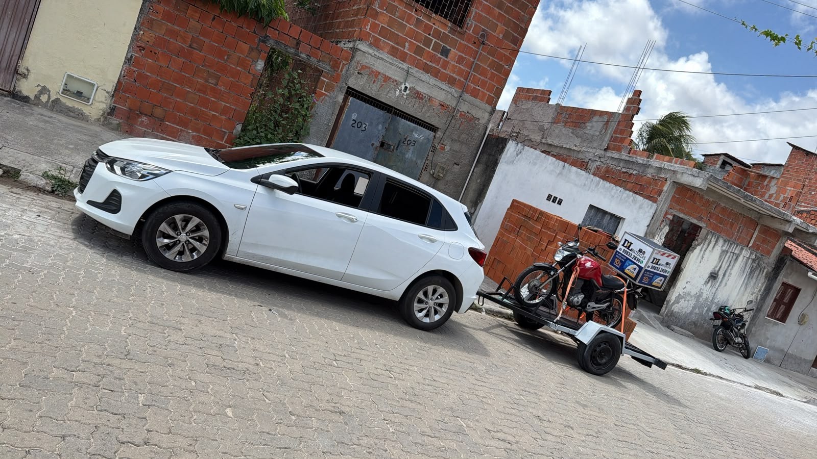 Chevrolet Onix branco da DL com moto e caixa DL Baterias na carretinha